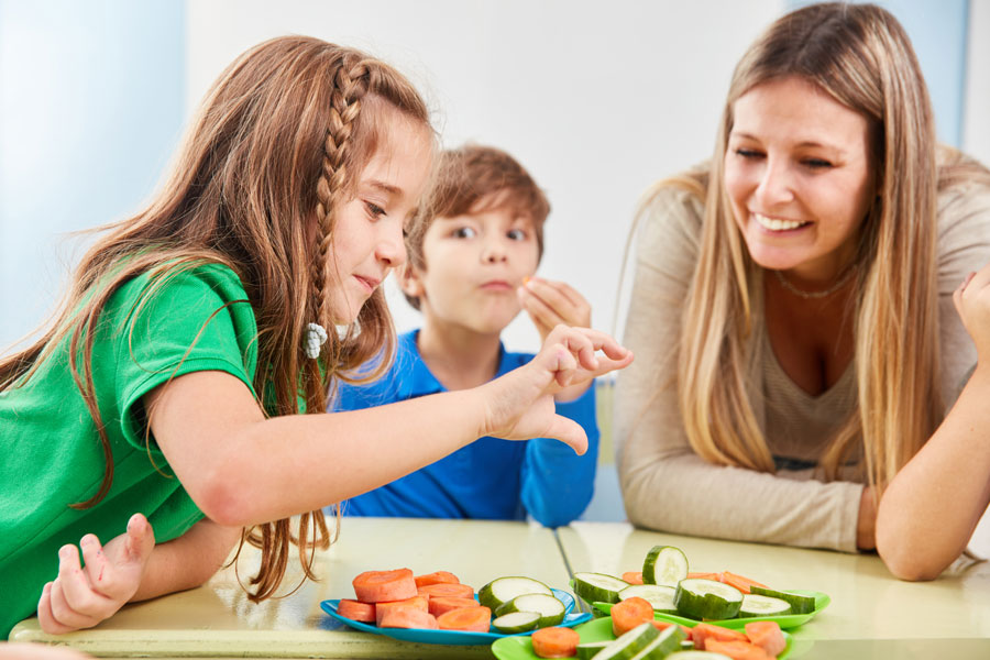 Family of 3 eating cucumbers and carrots