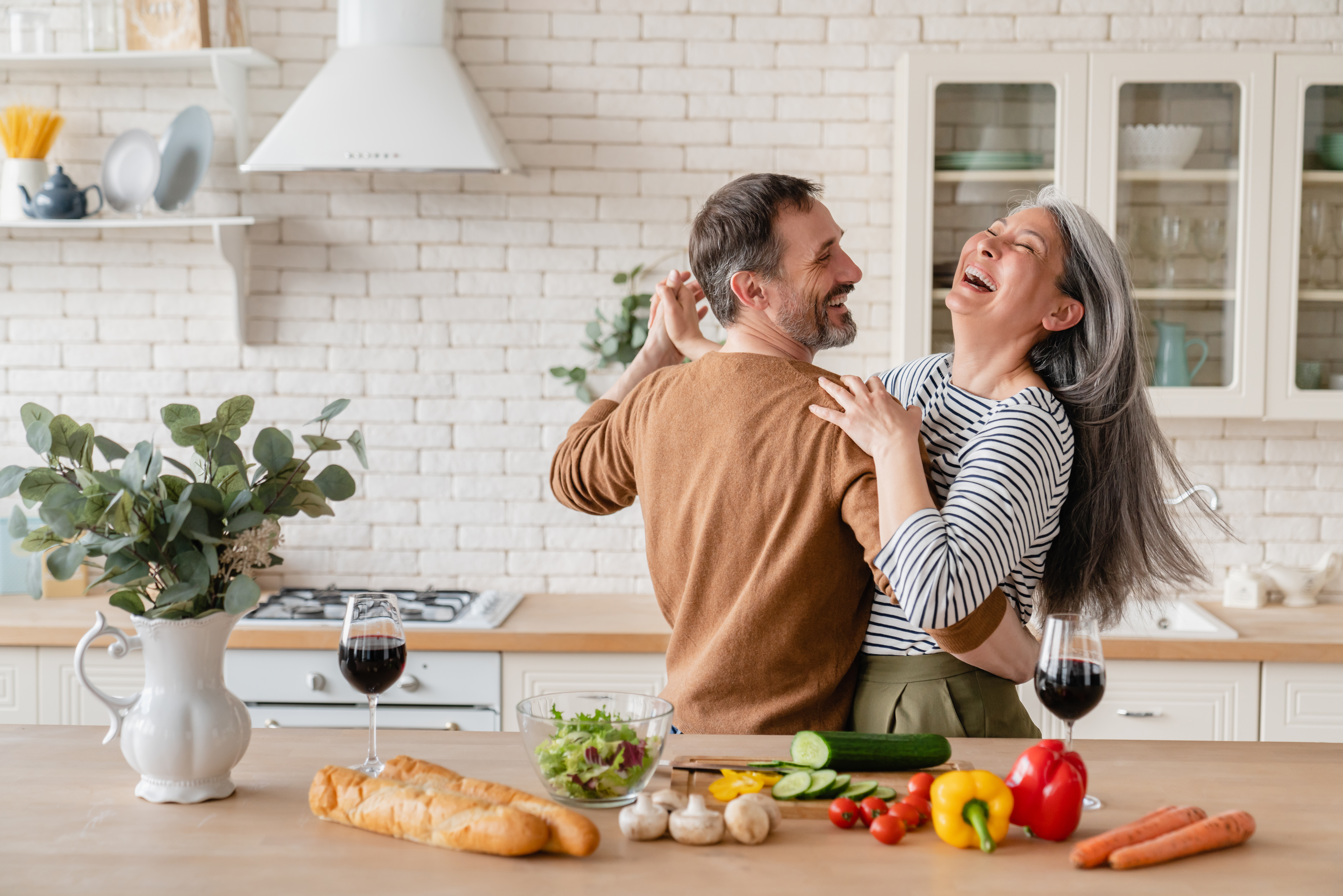 Cheerful middle-aged couple dancing while preparing a meal together